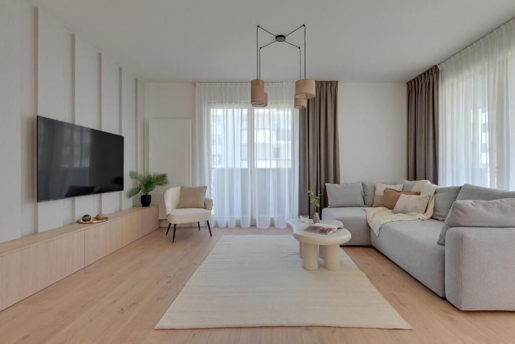 Un salon moderne avec un téléviseur à écran plat, un canapé, une table basse et une grande fenêtre avec des rideaux.