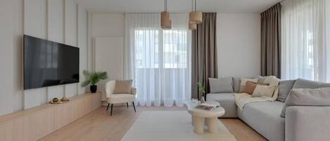 Una sala de estar moderna con una televisión de pantalla plana, un sofá, una mesa de centro y un ventanal con cortinas.