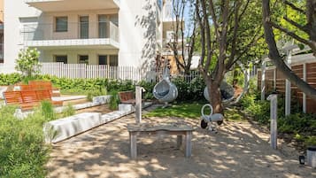 A courtyard with a wooden bench, a tree, and a white fence.