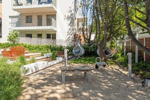 Un patio con un banco de madera, un árbol y una valla blanca.