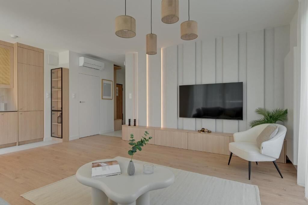 A modern living room with a flat-screen TV, a white armchair, and a coffee table.