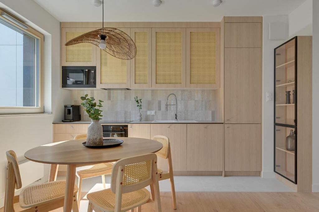Une cuisine moderne avec des meubles en bois clair, une table de salle à manger ronde entourée de chaises en osier et un luminaire suspendu.