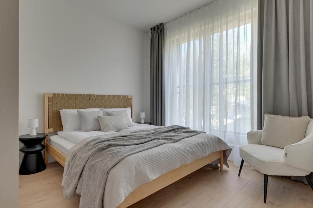 Een slaapkamer met een bed, een stoel, een nachtkastje en dunne gordijnen.