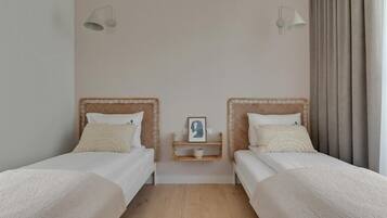 A room with two single beds, a small bedside table with a picture frame, and a wall-mounted light fixture.