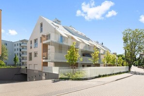Um edifício de apartamentos moderno com varandas, um caminho pavimentado e um portão.