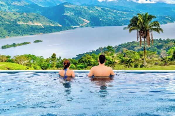 A couple in a swimming pool with a view of a lake and mountains.