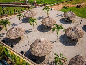 A beach area with thatched umbrellas and palm trees.