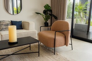 A modern living room with a beige sofa, a brown armchair, a black coffee table, and a large potted plant.