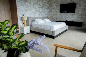 A modern bedroom with a bed, bedside tables, a TV, and a plant.