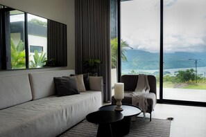 A modern living room with a sofa, a coffee table, and a view of a mountainous landscape through large windows.