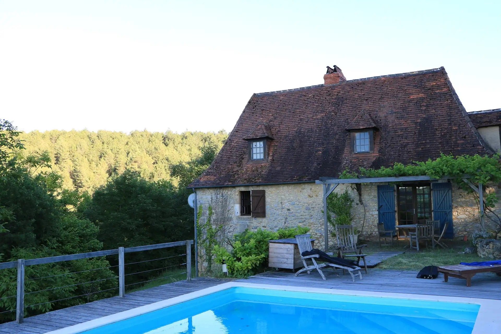 Une maison avec une piscine, une terrasse en bois et un mur en pierre.