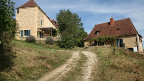 Ein Steinhaus, zu dem ein Feldweg durch üppiges Grün führt.