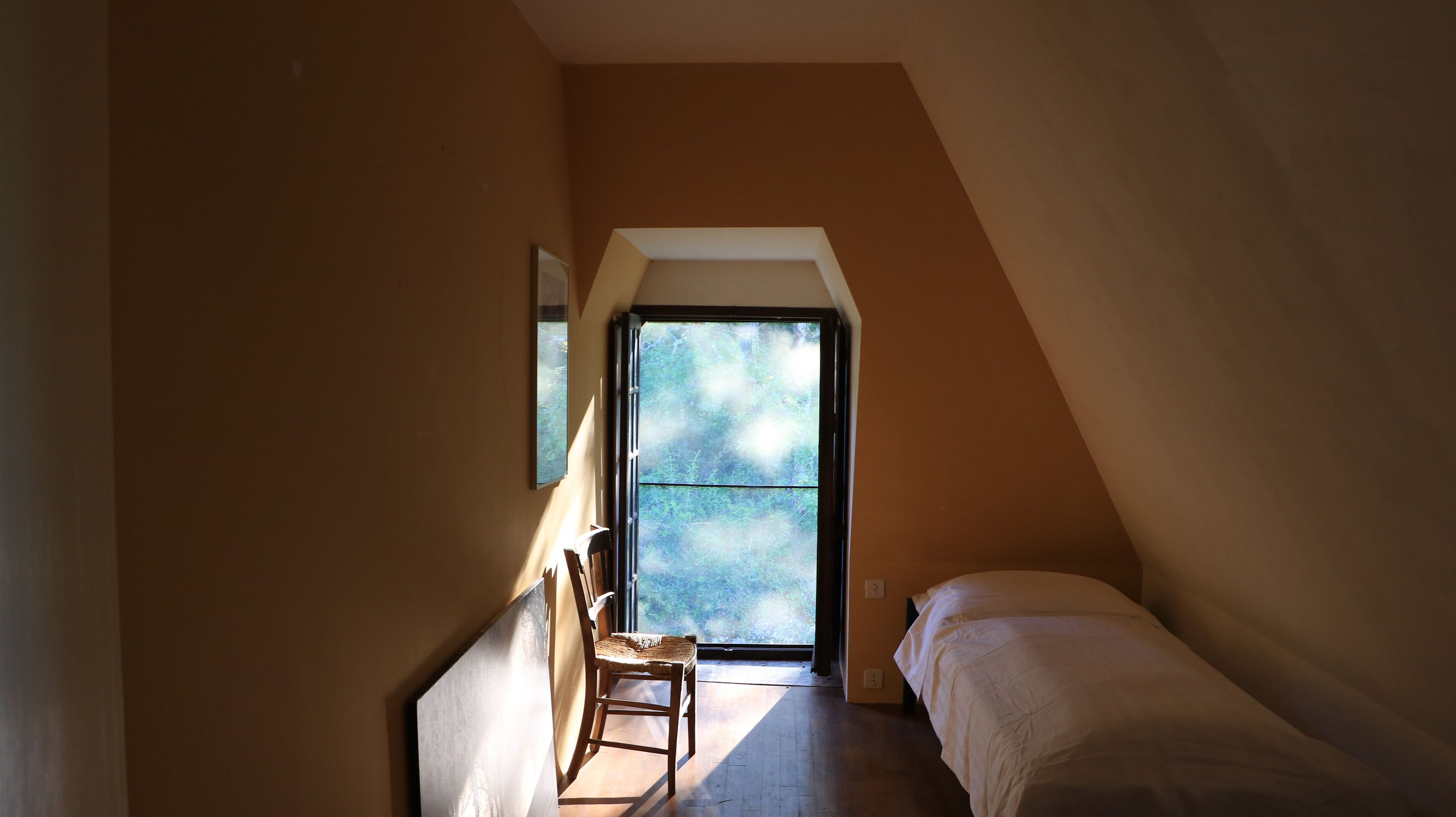 Una habitación pequeña con cama, una silla y un ventanal grande.