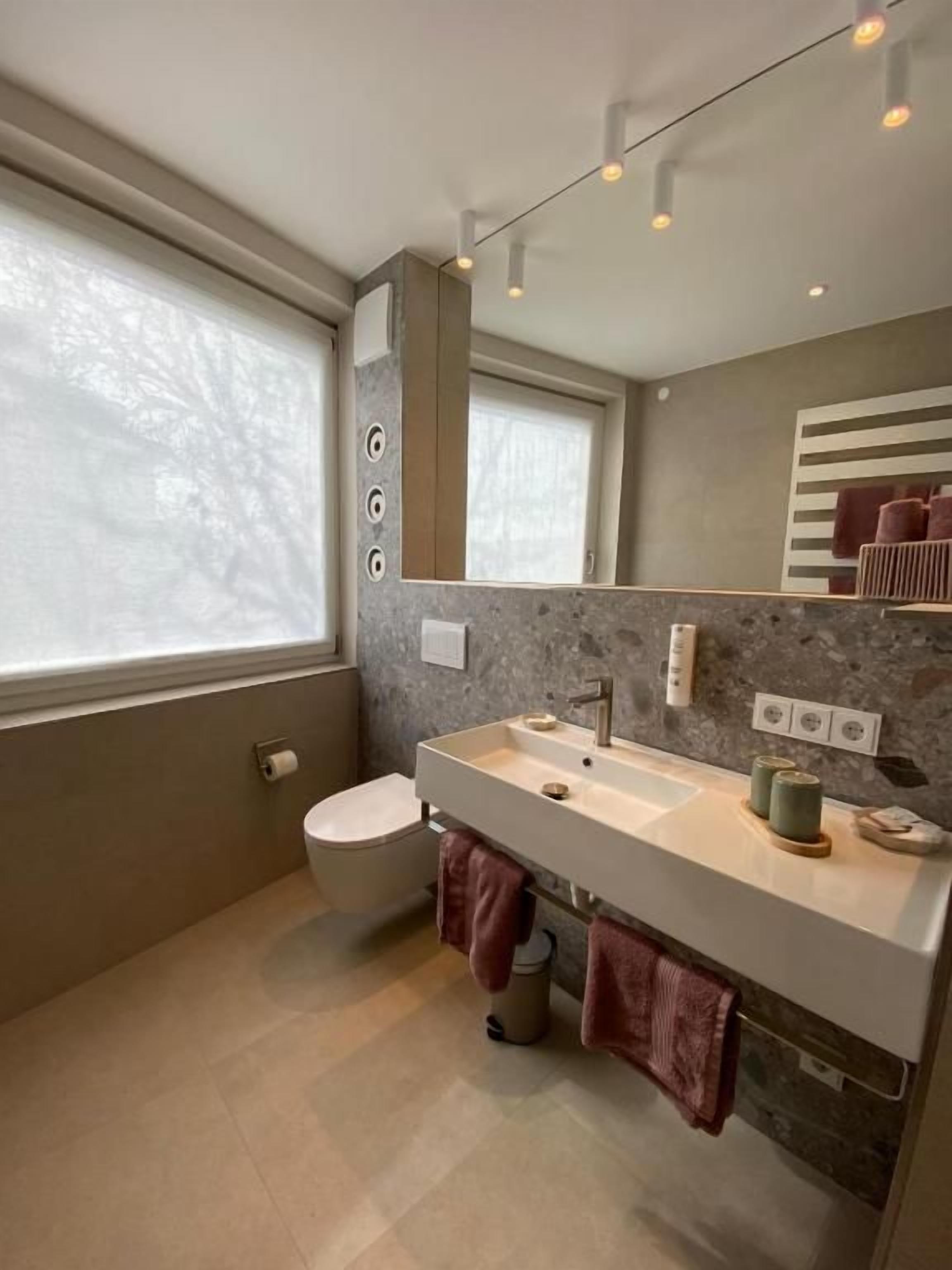 Une salle de bain moderne avec un grand miroir, un meuble-lavabo à deux vasques et des toilettes.