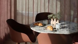 A dining area with a round table, chairs, a hanging light fixture, and a window with curtains. - Rex Palast (Memmingen)