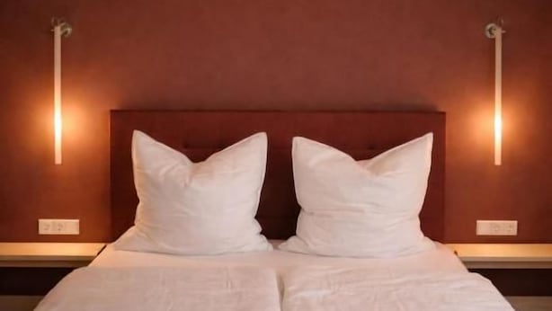 A double bed with a wooden headboard, two bedside tables, and wall-mounted lamps. - Rex Palast (Memmingen)