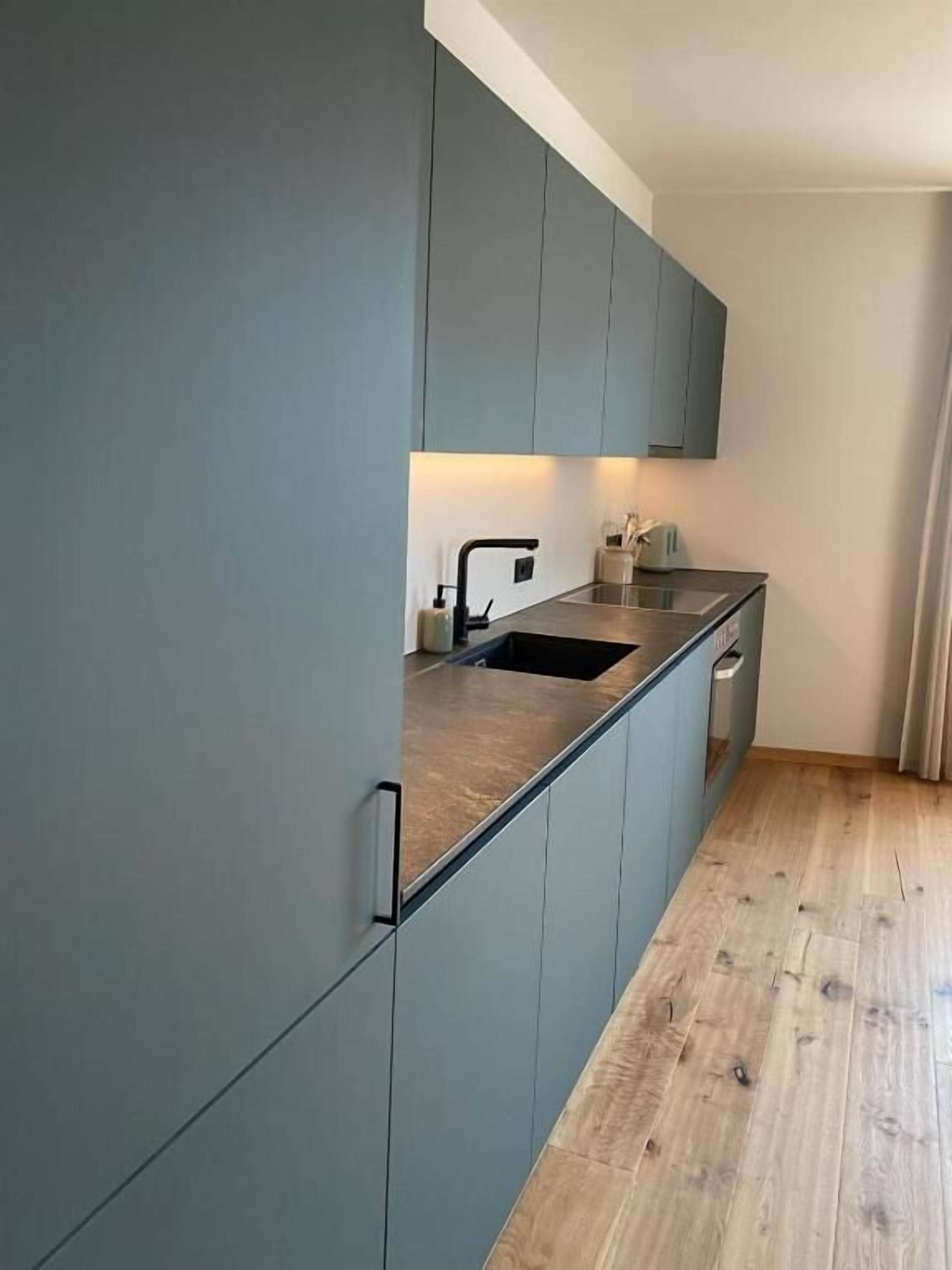 A modern kitchen with grey cabinets, a wooden countertop, and a black faucet.