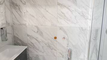 A bathroom with marble tiles, a white sink, and a shower area.