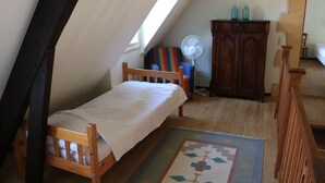 A small, cozy room with a sloped ceiling, a single bed, a wooden dresser, and a small fan. - Holiday Home 'Les Essarts La Maison' with Shared Pool, Private Terrace and Wi-Fi (Plazac)