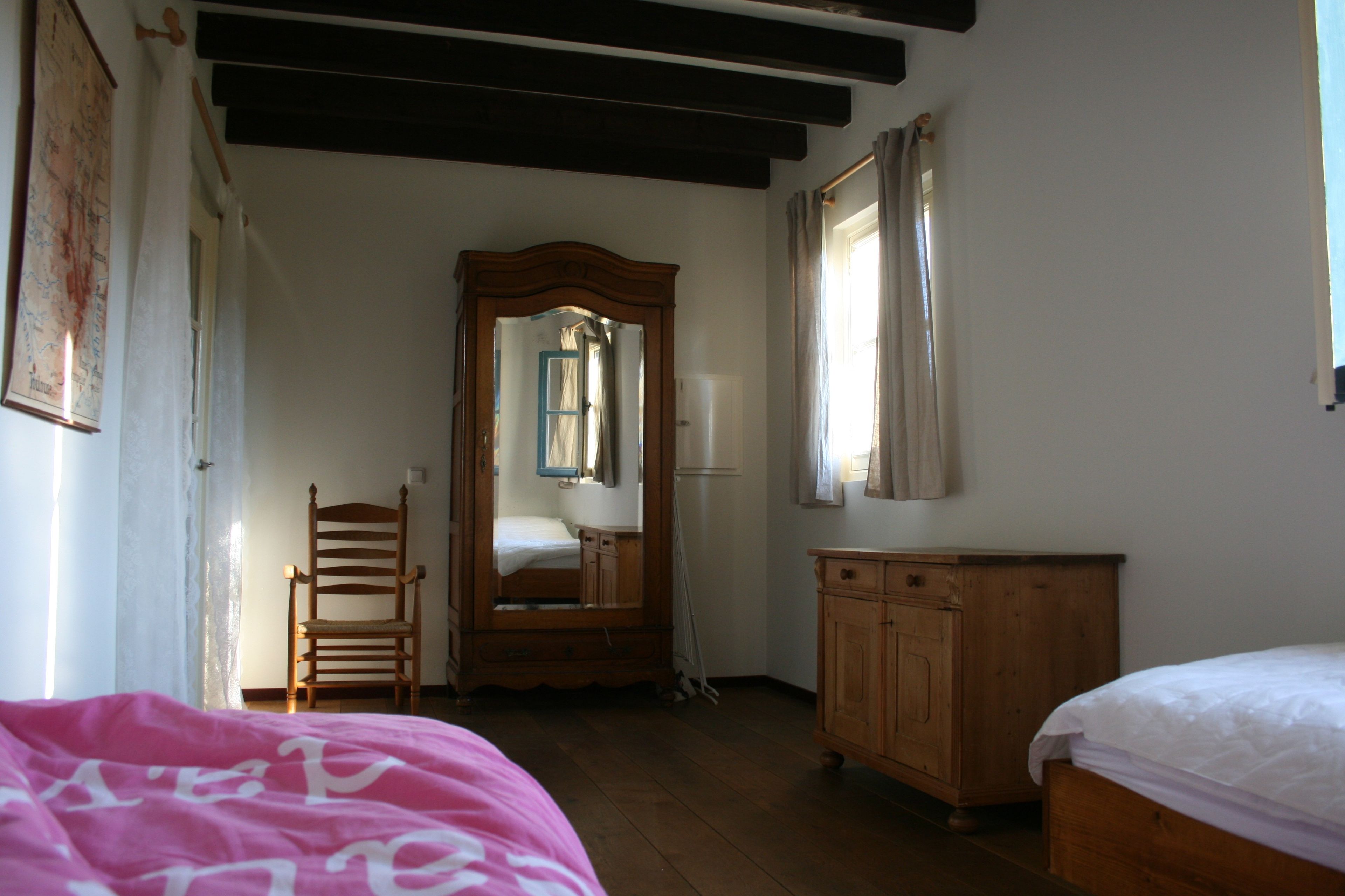 Une pièce comprenant une armoire en bois, un miroir, un lit et une chaise.