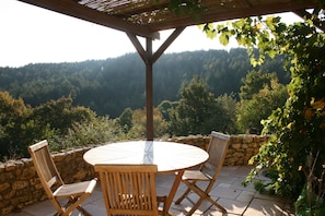 Ein Sitzbereich im Freien mit einem runden Tisch und vier Stühlen, umgeben von einer Steinmauer und einer Holzhütte.