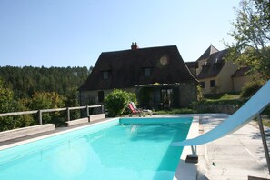 A swimming pool with a slide, surrounded by a wooden deck and a stone wall.
