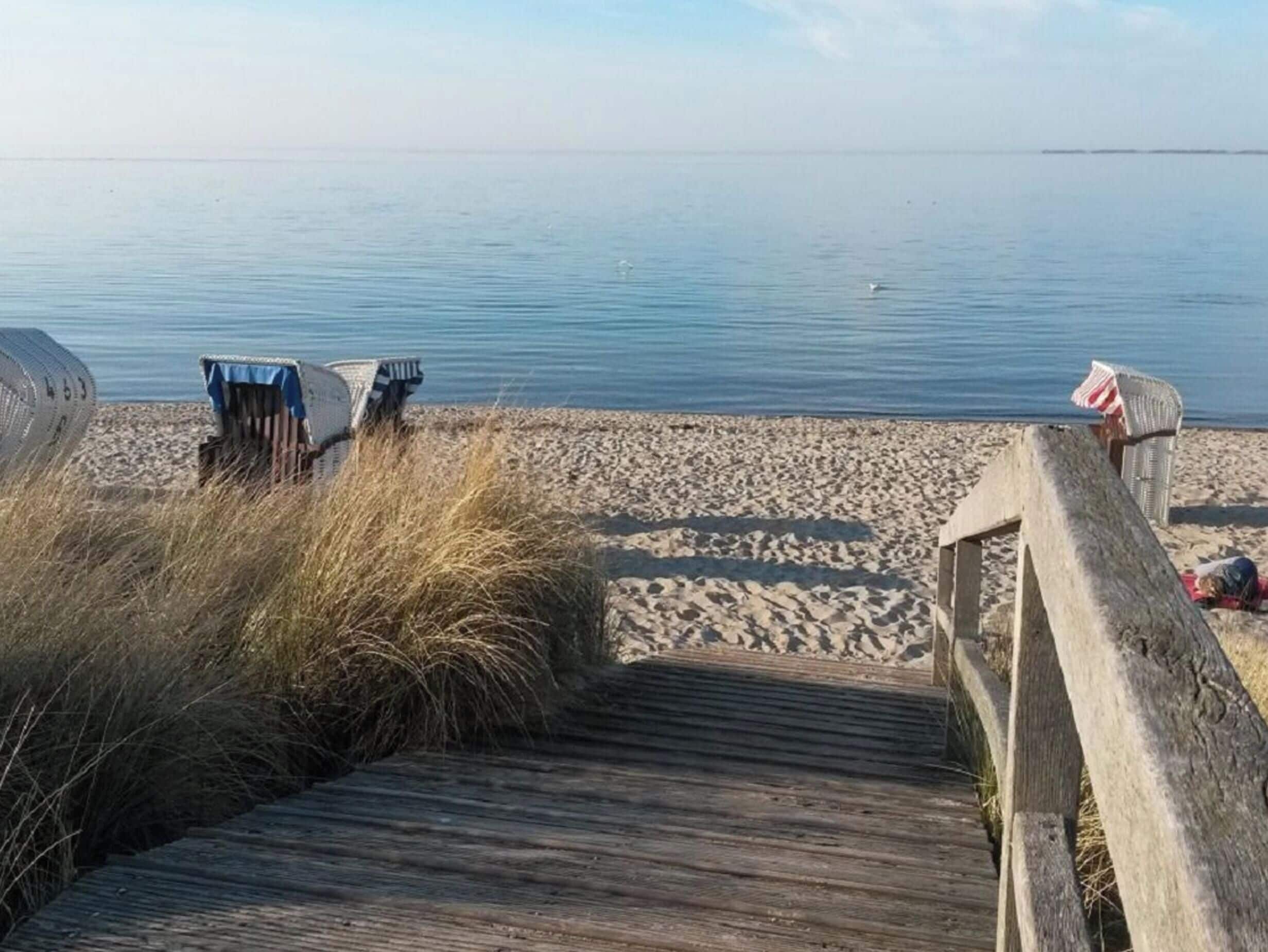 Une promenade en bois mène à une plage de sable fin, avec une étendue d’eau calme en arrière-plan.