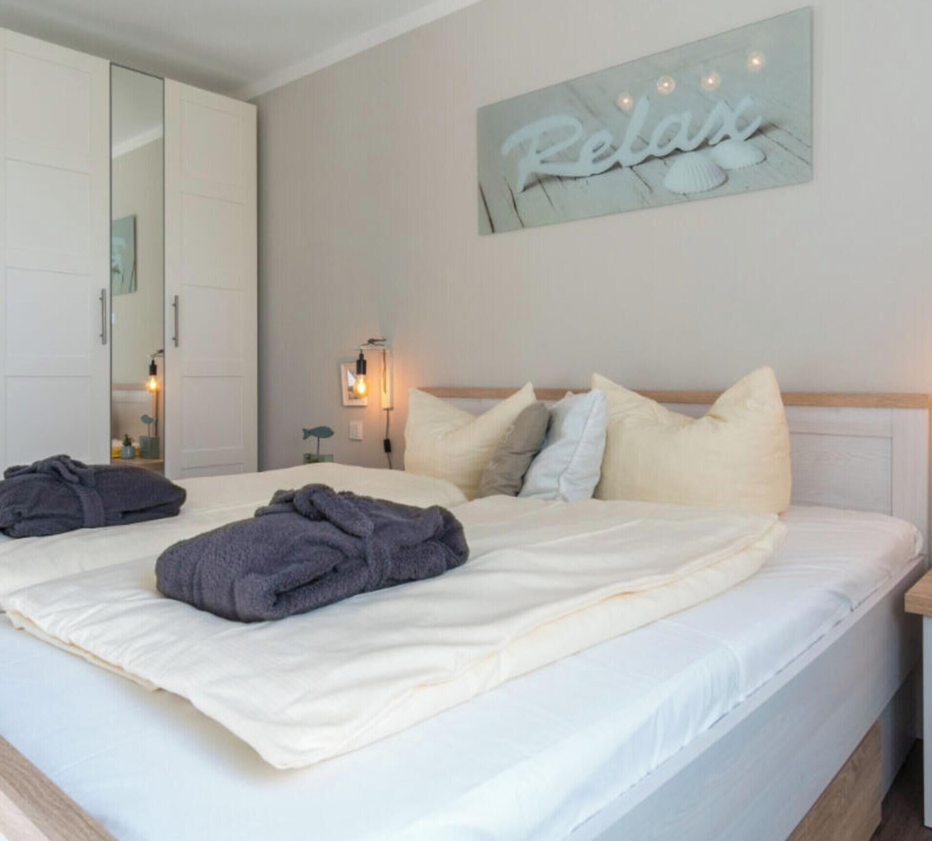 A hotel room with a bed, pillows, a bedside table, a wall-mounted light, and a mirror.