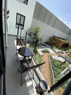 Ein moderner Balkon mit Glastrennwand, einem Esstisch mit Stühlen und Blick auf einen angelegten Garten.