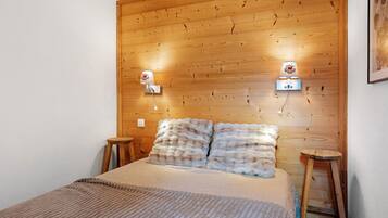 Een slaapkamer met een houten hoofdeinde, twee wandlampen, een bed met een zachte deken en twee houten krukjes.