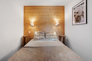 Un dormitorio con cabecera de madera, dos lámparas de noche, una cama con una manta texturizada y un cuadro en la pared.