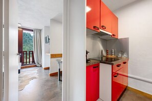 A modern kitchen with red cabinets, a stainless steel stove, and a window overlooking a forested area. - “Bellecôte” Apartment with Mountain View and Balcony (La Plagne Tarentaise)