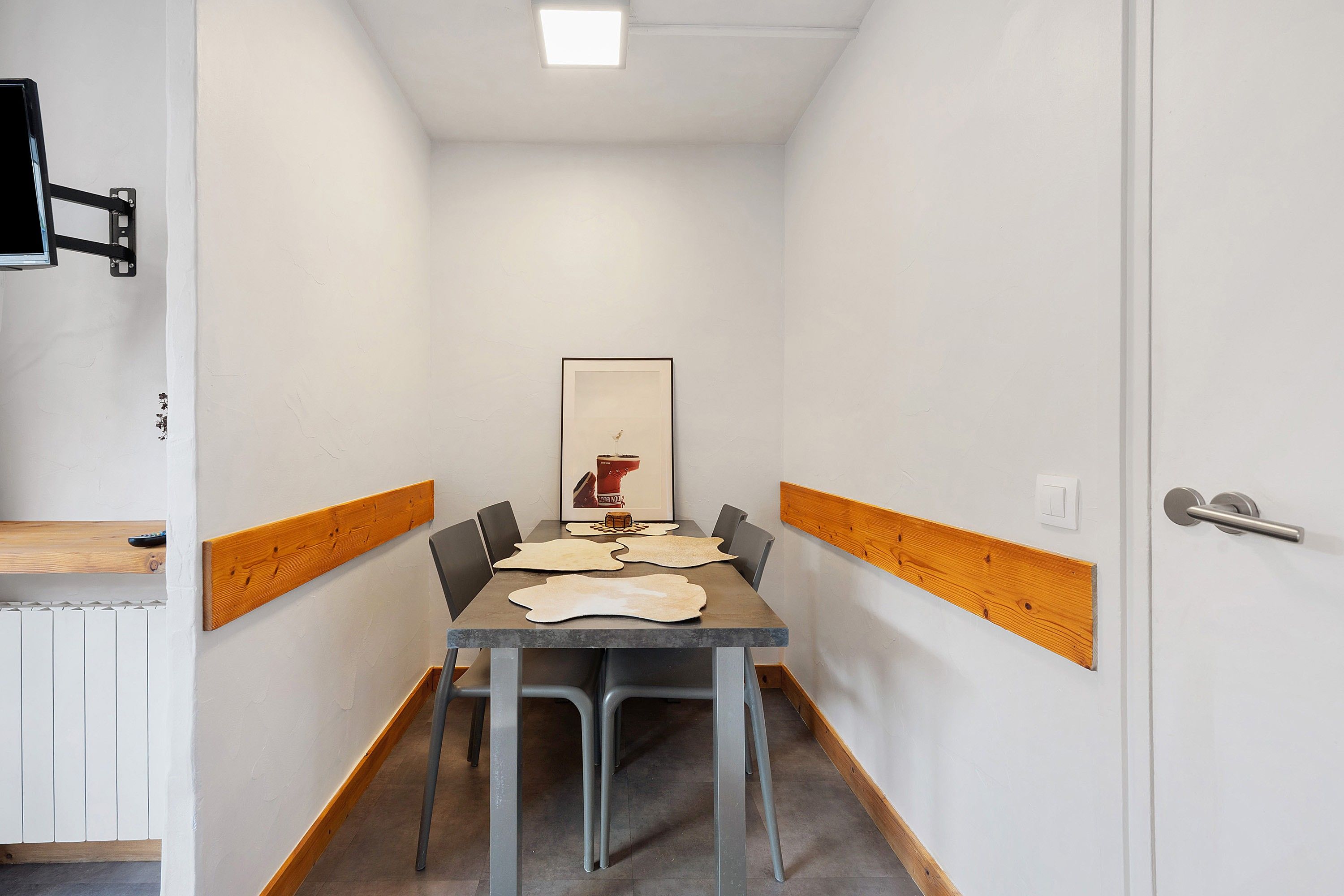 Un couloir étroit avec une table et des chaises, un tableau encadré au mur et une porte dotée d’une poignée.