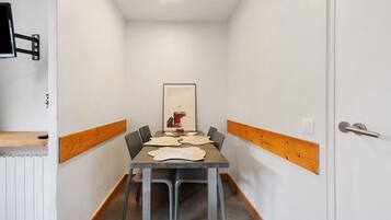 Un couloir étroit avec une table et des chaises, un tableau encadré au mur et une porte dotée d’une poignée.