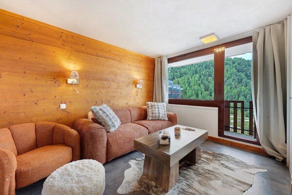 Una sala moderna con pared de madera, un juego de sofá, una mesa de centro y vista a un área boscosa a través de un ventanal grande.