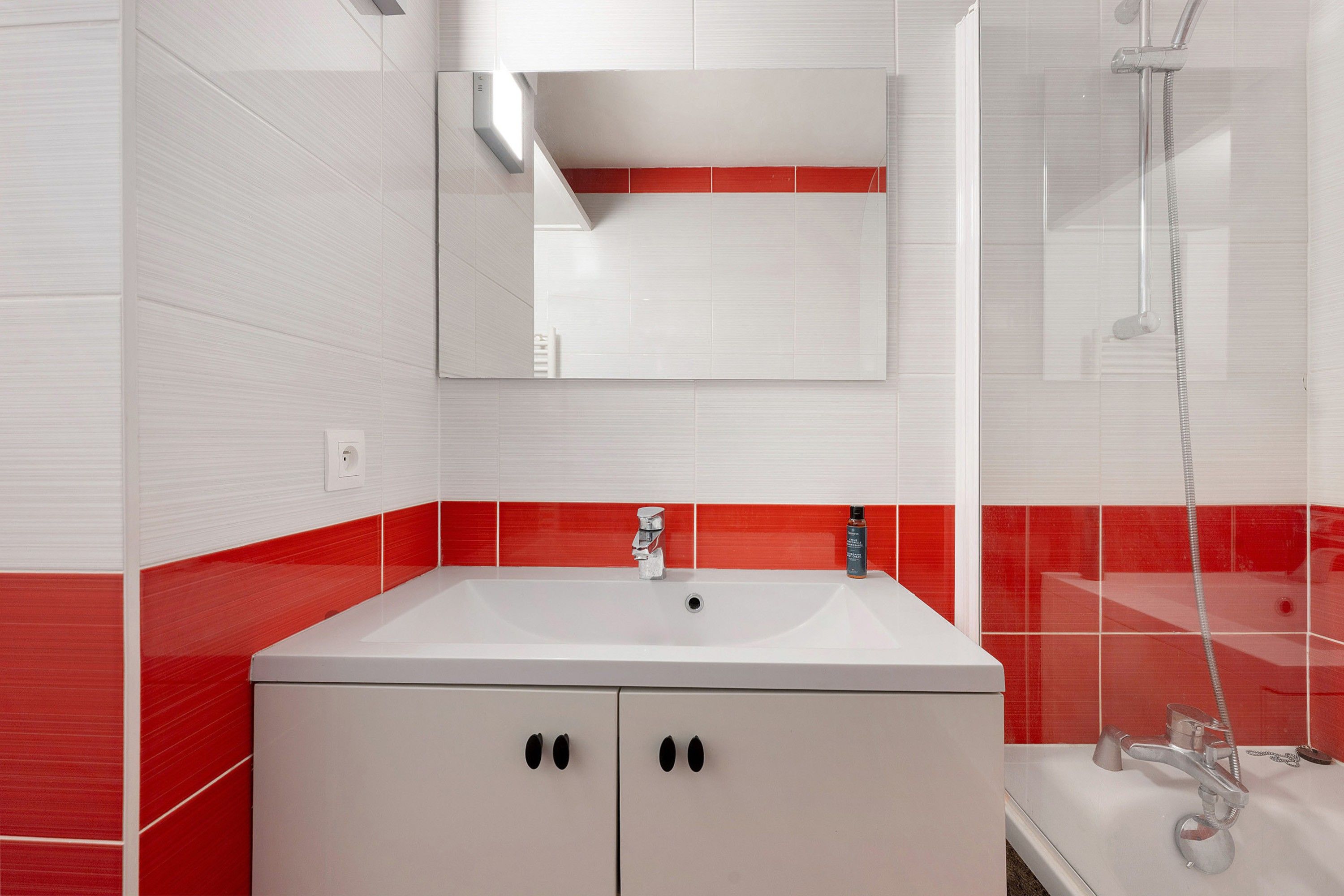 Een badkamer met een wit wastafel, een spiegel en een douche.