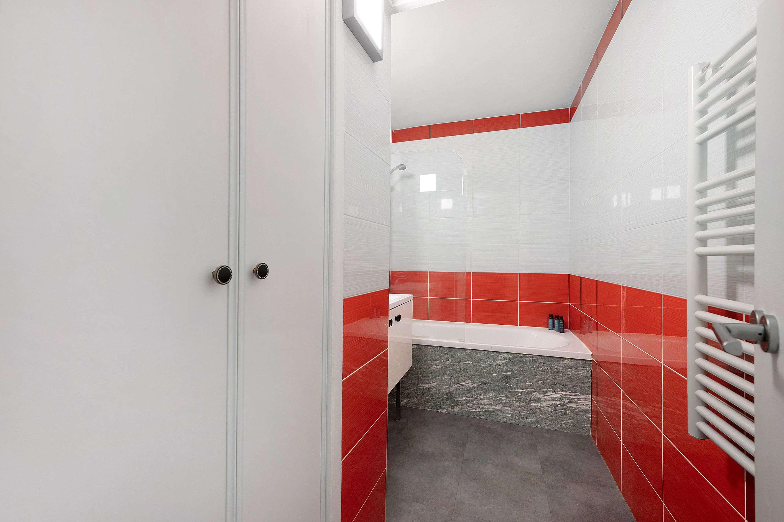 A bathroom with a white door, red-tiled walls, a white sink, and a shower area.