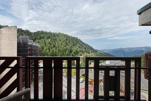 A balcony with a view of a forested hillside and distant mountains.