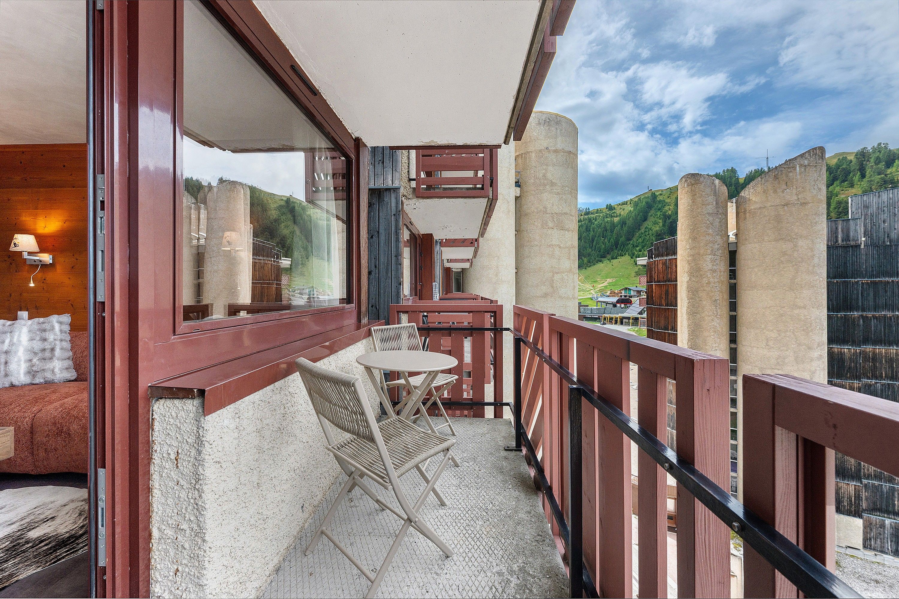 A balcony with a table and chairs, a view of a green landscape, and a wooden railing.