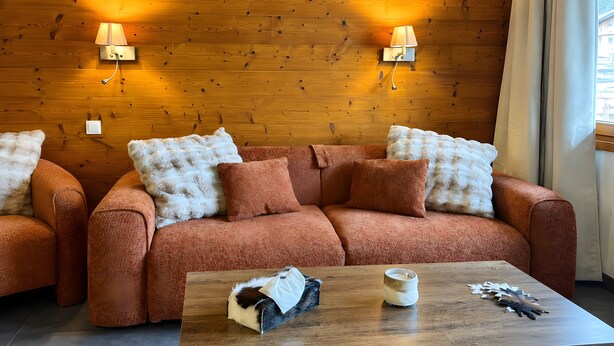 Un accogliente soggiorno con parete in legno, due divani con cuscini soffici, un tavolino da caffè con oggetti decorativi e lampade a parete.