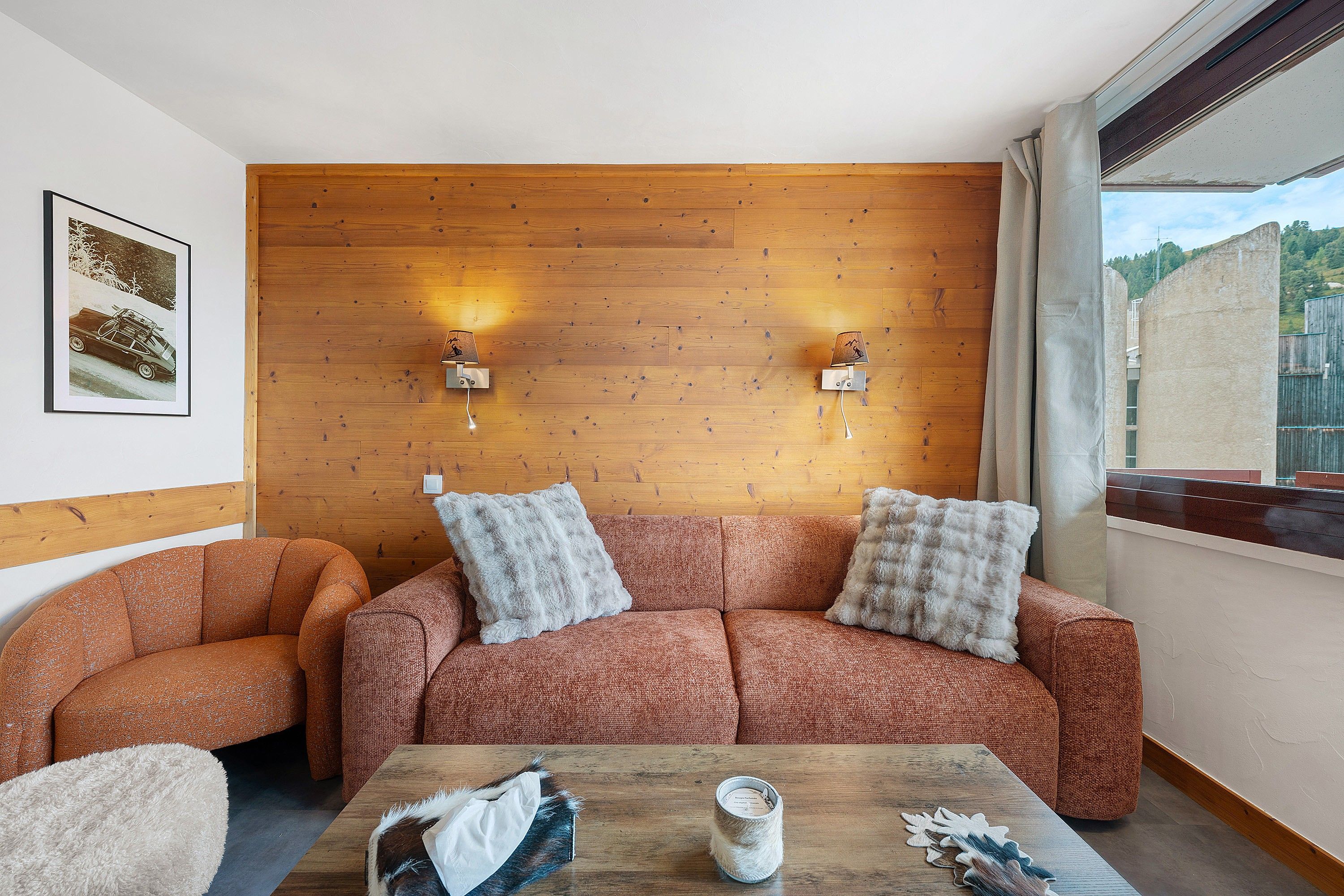 Une pièce chaleureuse avec un mur en bois, deux lampes fixées au mur, un canapé et une table basse.