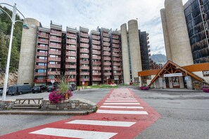 Un hotel con un paso de peatones rojo, una zona de estacionamiento y un edificio con varios balcones.