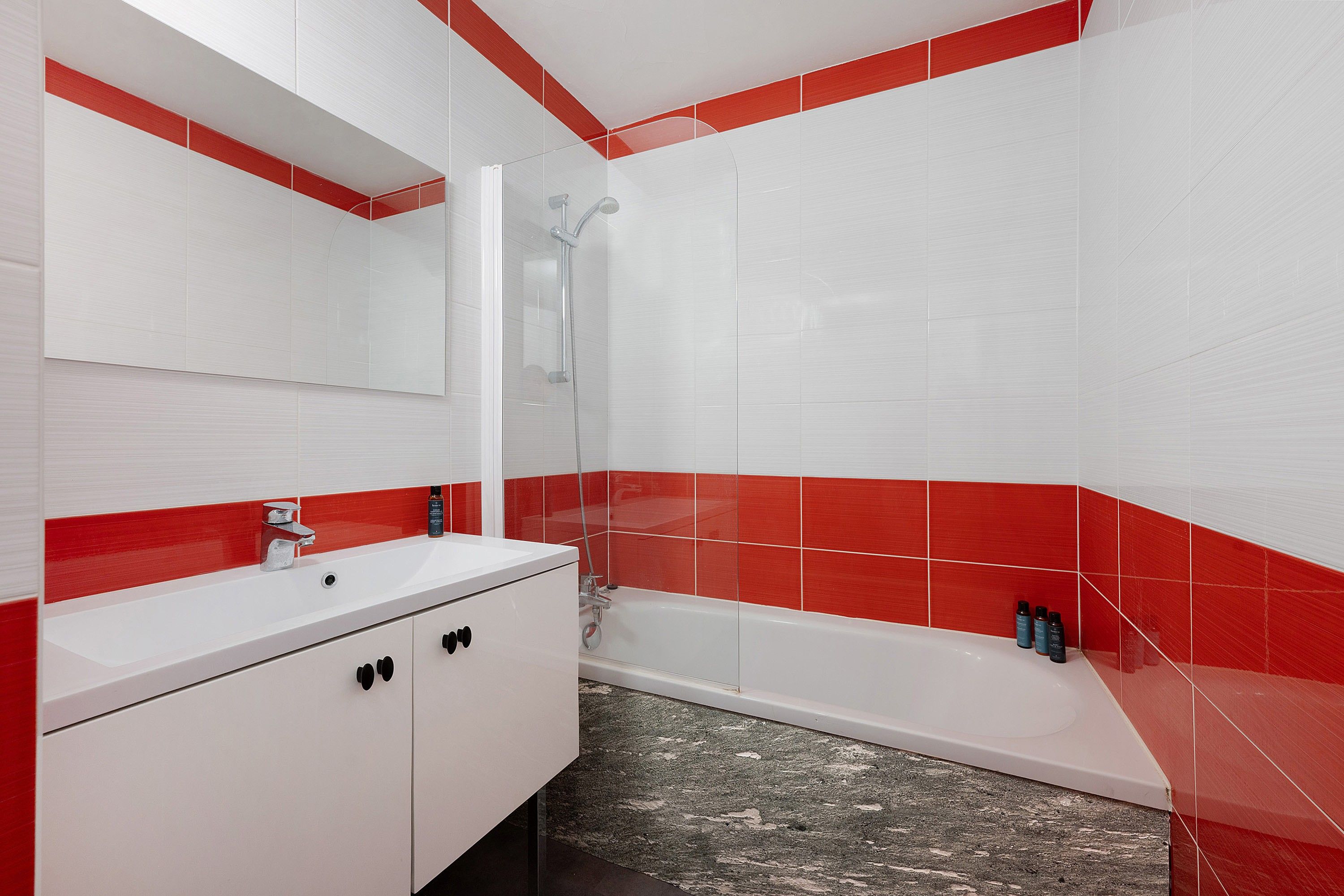 Une salle de bain avec un lavabo blanc, un miroir, une douche et des murs recouverts de carreaux rouges.