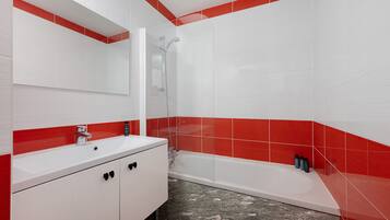 Une salle de bain avec un lavabo blanc, un miroir, une douche et des murs recouverts de carreaux rouges.
