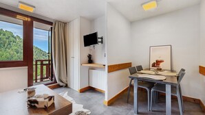 Habitació moderna amb taula de dinar, cadires, televisió plana penjada a la paret i finestra amb vista a una zona boscosa.