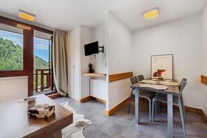 Una habitación moderna con una mesa de comedor, sillas, un televisor de pantalla plana en la pared y un ventanal con vistas a un área boscosa.
