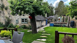 Un jardin avec un mur en pierre, une terrasse en bois et un chemin en pierre.