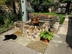 A brick outdoor kitchen with a gas stove, surrounded by potted plants and a dog lying on the ground.