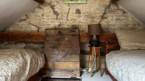 Une chambre mansardée au charme rustique, avec des murs en pierres apparentes, des poutres en bois et un lit en mezzanine.