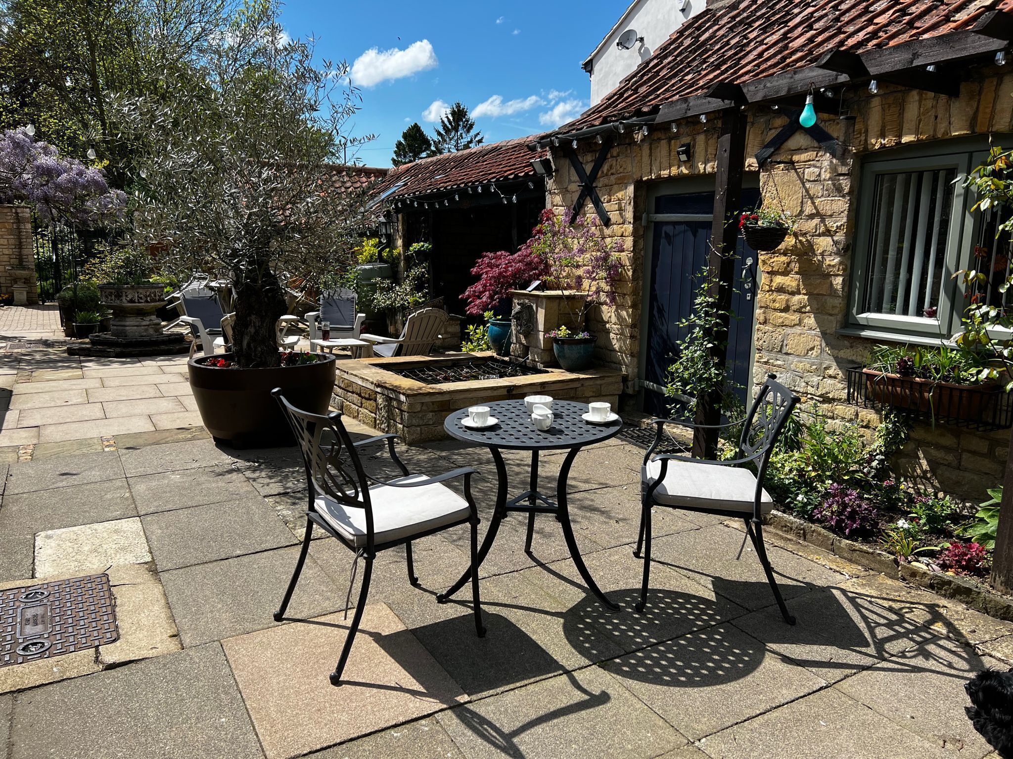 An outdoor patio with a stone table and two chairs, surrounded by potted plants and a stone wall.